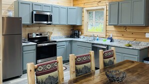 A cozy cabin-style kitchen with wooden walls, a dining table with chairs, and modern appliances. - Misty Mountain View @Smokies  #Xplorietickets:  Explore More, Experience More!! (Gatlinburg)
