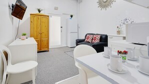 A modern, well-lit room with a white desk, a black leather sofa with a red and white pillow, a wooden wardrobe, a white cabinet, and a mounted television. - Azure Beach Hotel (Bournemouth)