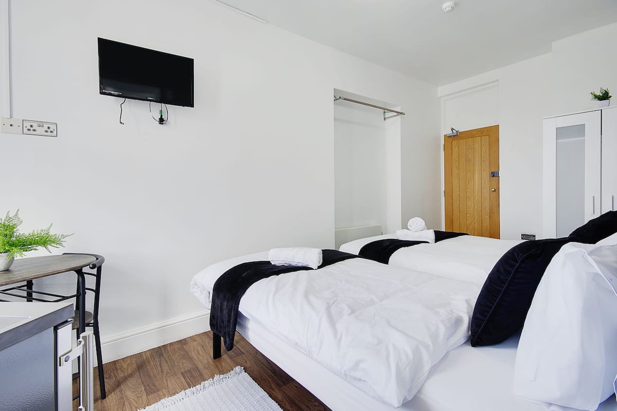 A hotel room with a bed, a desk, a TV mounted on the wall, a wooden door, and a white wardrobe.