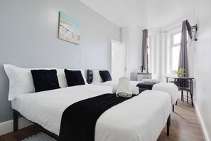 A hotel room with two beds, a desk, a chair, a potted plant, and a window with curtains. - Azure Beach Hotel (Bournemouth)