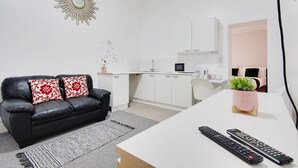 A modern living room with a black leather sofa, a white table, and two remote controls. - Azure Beach Hotel (Bournemouth)