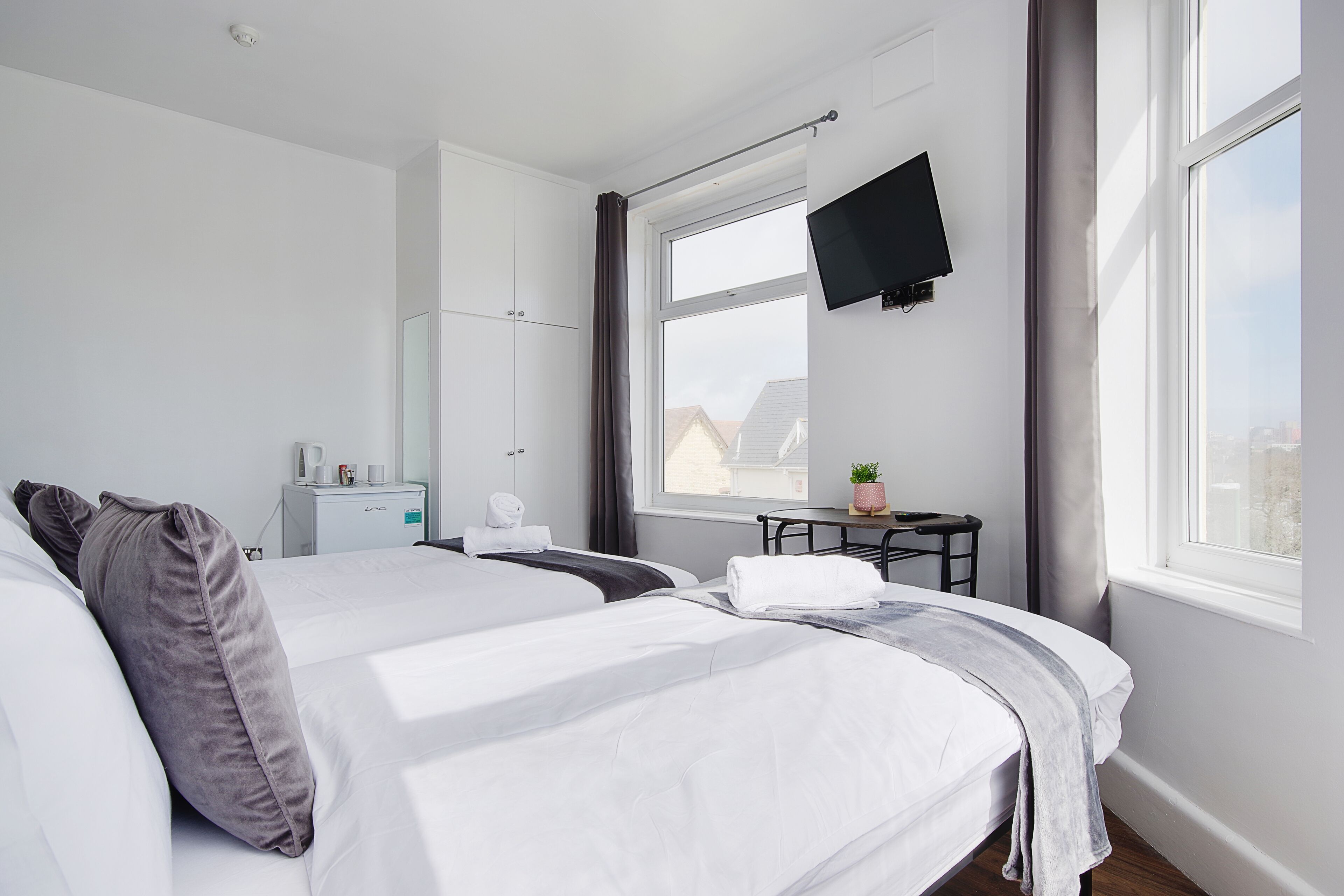 A hotel room with two beds, a desk, a TV, and a window with a view of buildings.