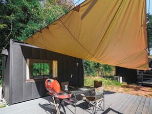 A small outdoor seating area with a table and chairs, a grill, and a large canopy providing shade. - Bulls Camp (Narusawa)