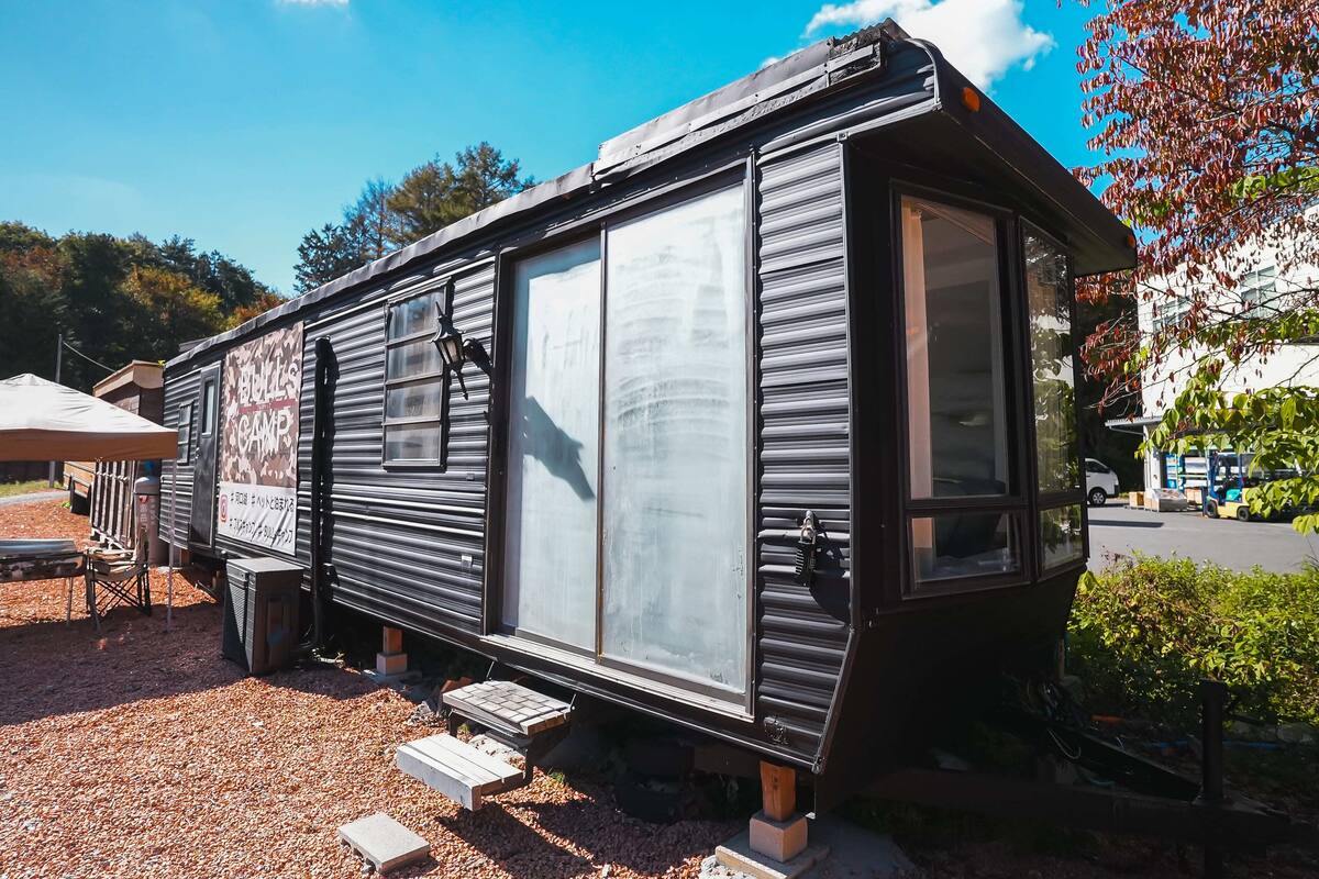 A mobile home with a large window, a small porch, and a sign advertising a camp.