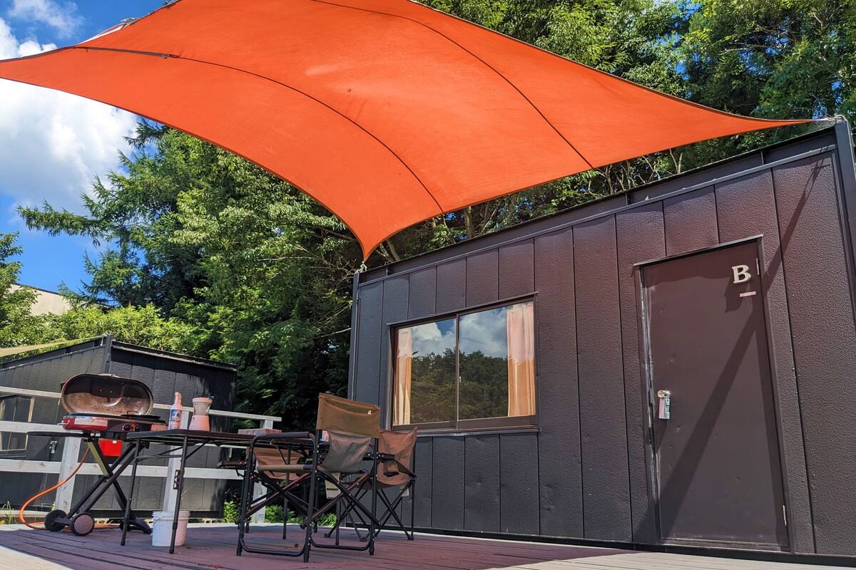 A wooden deck with outdoor furniture, a large orange shade, and a building with a window and a door marked 'B'.