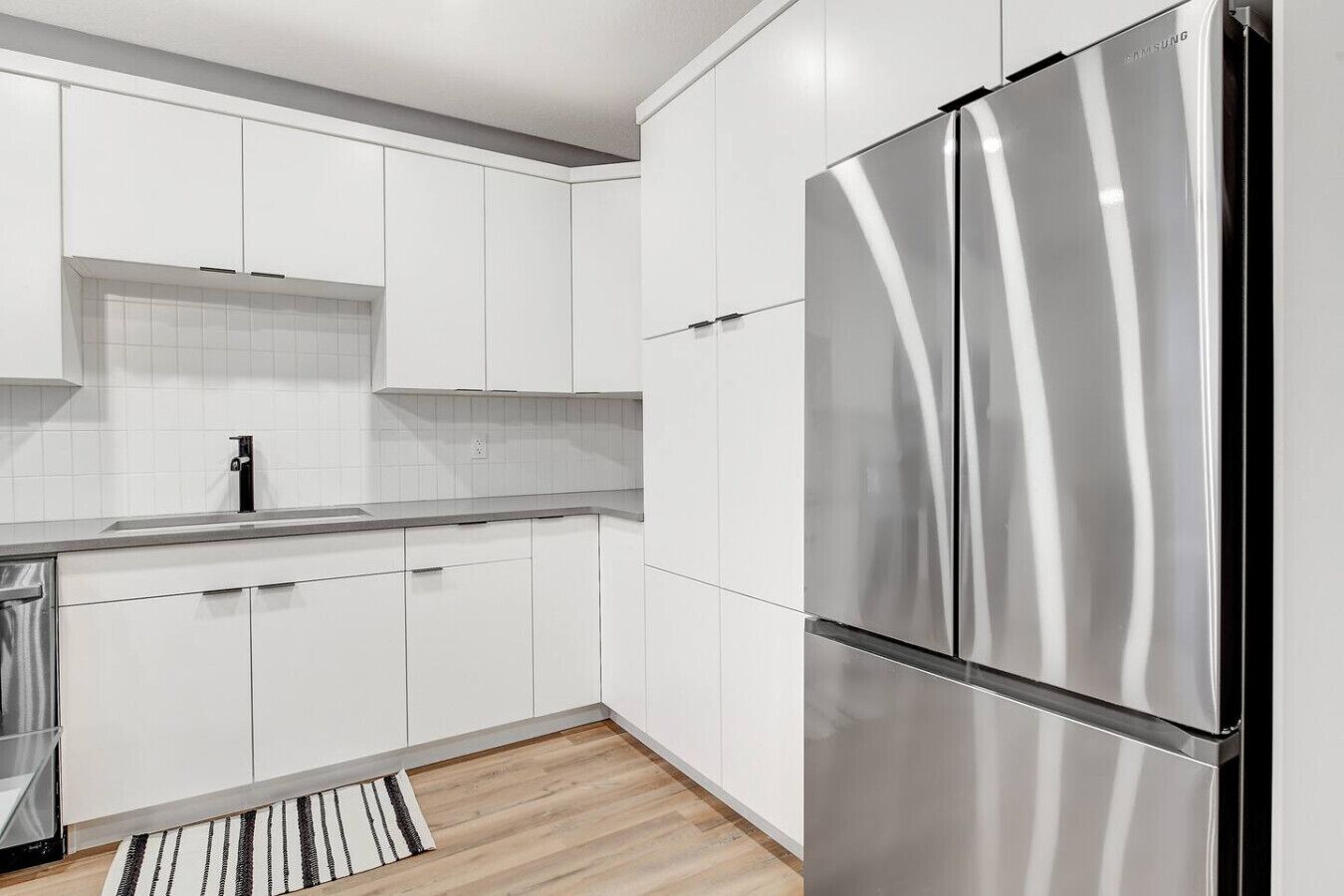 A modern kitchen with white cabinetry, a stainless steel refrigerator, and a striped rug.