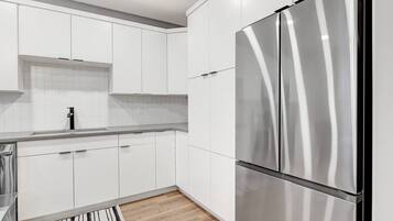 A modern kitchen with white cabinetry, a stainless steel refrigerator, and a striped rug.