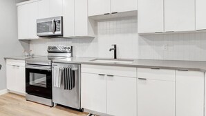 Een moderne keuken met witte kasten, roestvrijstalen apparatuur en een betegelde spatwand.