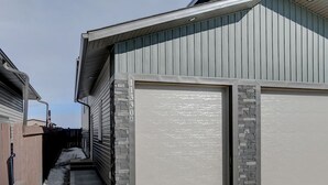 Een garage voor twee auto's met een geaccentueerde stenen muur, een metalen dak en een heldere lucht.
