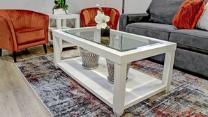 Een moderne woonkamer met een salontafel met glazen blad, een vloerkleed met patroon en een grijze bank.