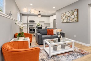A modern living room with a grey sofa, orange armchair, and a glass coffee table. - Quiet 2BR Suite · Garage · Near Hospital & Costco (Grande Prairie)