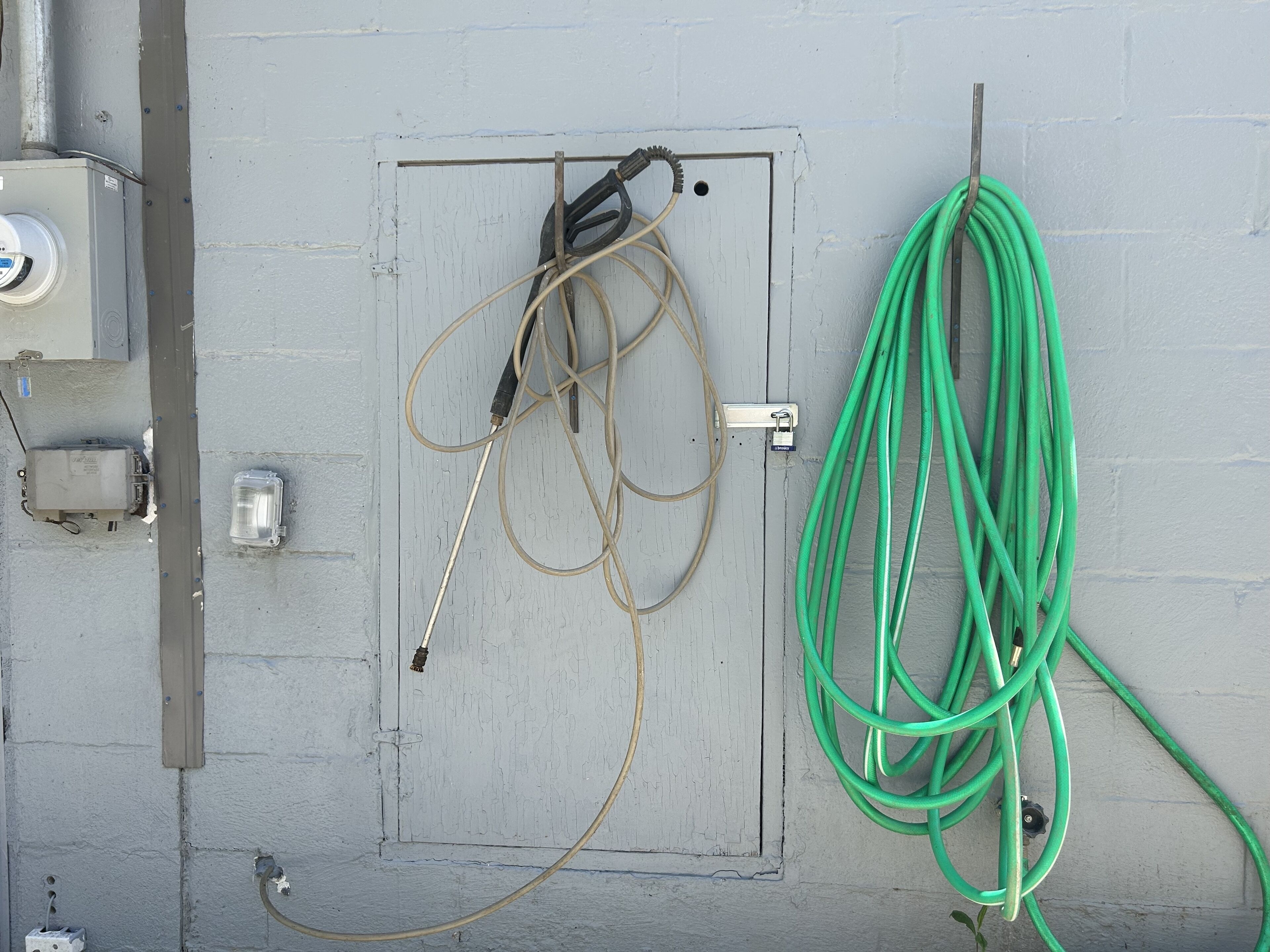Une pièce utilitaire contenant des panneaux électriques, une porte et un tuyau d’arrosage vert enroulé sur le mur.