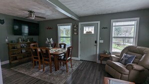 A dining area with a wooden table and chairs, a small rug, and a television mounted on the wall. - Trail Riders Retreat! Hatfield McCoy Trails. Private Pool. Loads of Parking!  (Williamson)