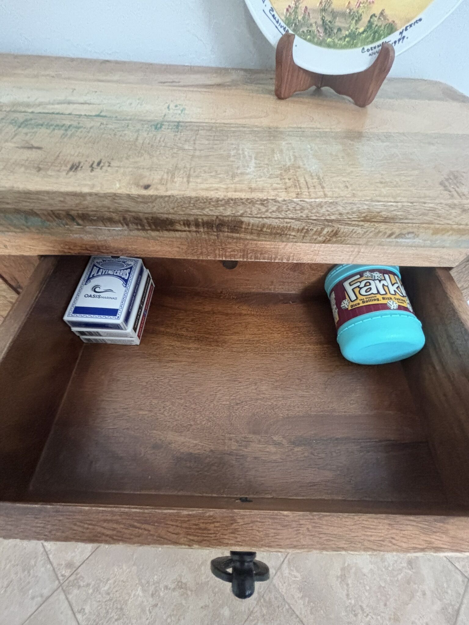 Un cassetto di legno con una maniglia nera, contenente un mazzo di carte da gioco e un barattolo con i dadi di Farkle.