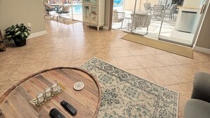 A spacious living area with a wooden coffee table, a patterned rug, and a view of a pool and outdoor seating area. - Summer vacation, dream destination w heated pool boat dock kids and pets welcome (Cape Coral)