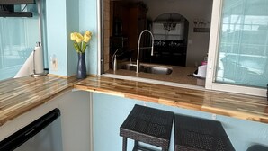 A compact kitchen with a wooden countertop, two black stools, a sink, and a decorative fish wall art piece. - Summer vacation, dream destination w heated pool boat dock kids and pets welcome (Cape Coral)