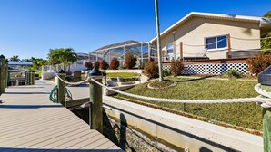 A coastal property with a wooden deck, a glass-enclosed patio, and a well-maintained lawn. - Summer vacation, dream destination w heated pool boat dock kids and pets welcome (Cape Coral)