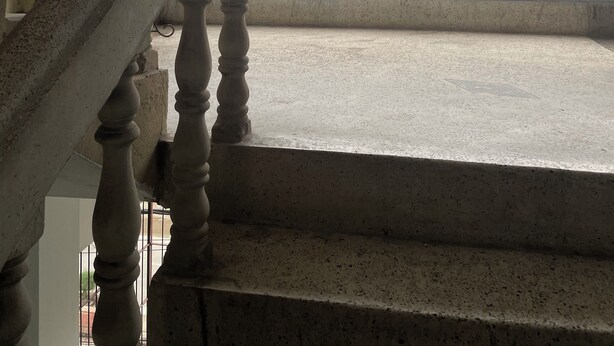 A staircase with a metal railing leading to a balcony with a view of a building through a barred window. - Hotel Sharnali (Khulna)