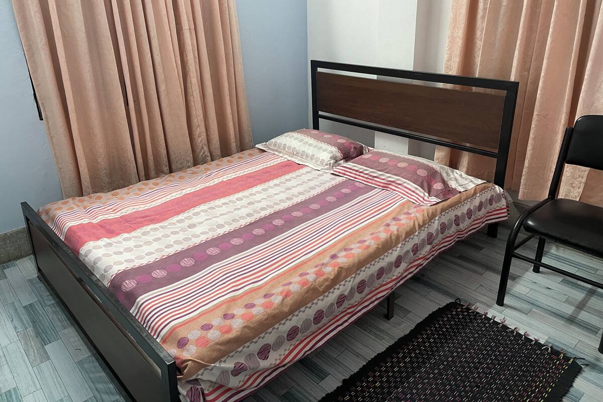 A single bed with a patterned bedspread, a wooden headboard, and a black chair.