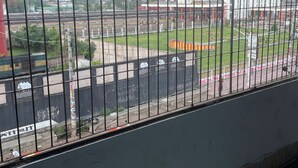 A view through a metal fence with a railway track and buildings in the background. - Hotel Sharnali (Khulna)