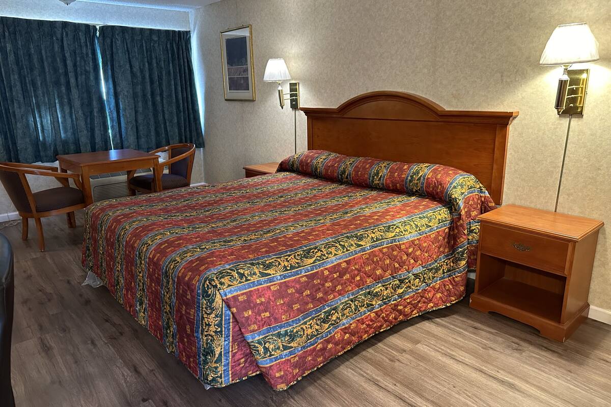 Camera d'albergo con un letto grande, una scrivania in legno, una sedia, un comodino e due lampade a parete.