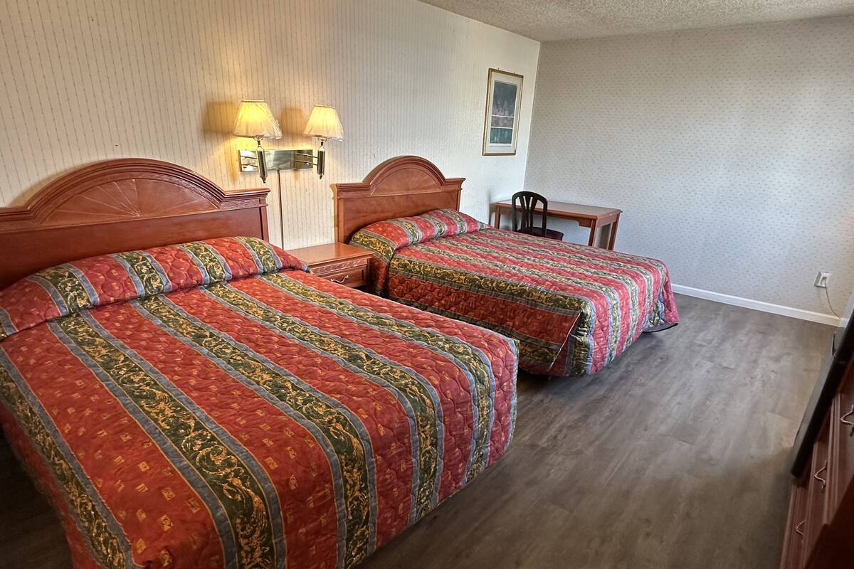 Una camera d'albergo con due letti, un comodino, una sedia e un piccolo tavolo.