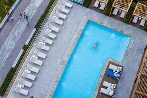 Luftaufnahme eines Schwimmbeckenbereichs mit Liegestühlen und einer Person, die schwimmt.
