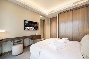 A hotel room with a bed, a desk, a mirror, and a wall-mounted TV displaying 'Stranger Things'. - NEW | 3BR Burj Fountain NYE View | Address (Dubai)