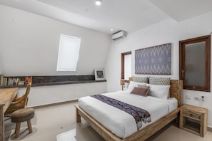 A modern bedroom with a wooden bed, a small wooden nightstand, a wicker chair, and a bookshelf. - Gajah Villa by Betterplace (Canggu)