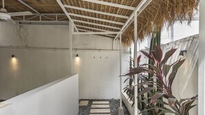 A covered walkway with a thatched roof, white walls, and a gravel path. - Gajah Villa by Betterplace (Canggu)