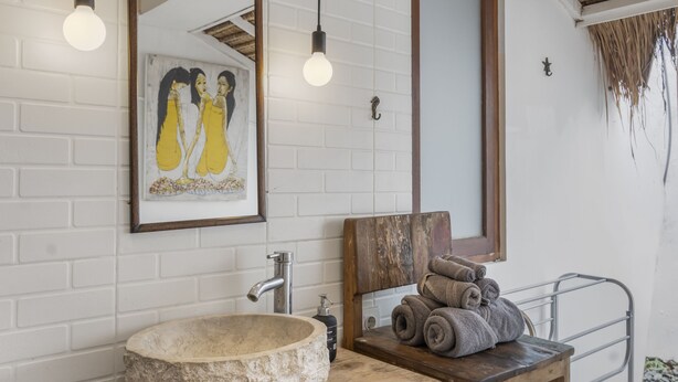 A bathroom with a white brick wall, a wooden vanity, a stone basin, a framed artwork, and a towel rack. - Gajah Villa by Betterplace (Canggu)