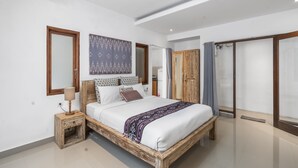 A modern bedroom with a wooden bed frame, a bedside table with a lamp, a large mirror, and a sliding door closet. - Gajah Villa by Betterplace (Canggu)