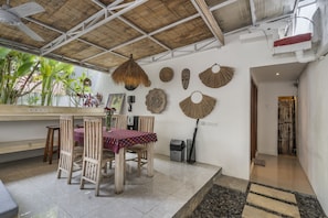A dining area with a table set for two, surrounded by wooden chairs, a thatched ceiling, and a variety of wall decorations including woven baskets and masks. - Gajah Villa by Betterplace (Canggu)