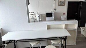 A modern kitchen with a white countertop, a microwave, and a sink. There are three white stools and a black metal table.