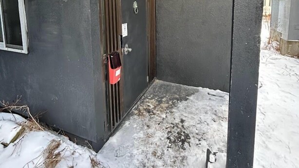 A narrow entrance with a metal door, a red bag hanging on the door handle, and a small sign above the door.
