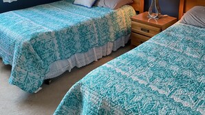 Et hotelværelse med to senge, et natbord med lampe, et billede på væggen og en aircondition.
