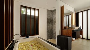 A modern bathroom with a large bathtub filled with flower petals, a wooden vanity, and a large mirror. - Jimbaran Bay Villas by Nakula (Kedonganan)