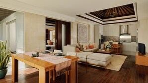 A modern living room with a wooden dining table, a sofa, and a kitchen area with a tiled backsplash. - Jimbaran Bay Villas by Nakula (Kedonganan)