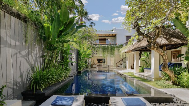 A serene pool area with lounge chairs, a thatched-roof structure, and lush greenery. - Jimbaran Bay Villas by Nakula (Kedonganan)