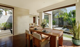 Un comedor moderno con una mesa y sillas de madera, un jarrón con flores y vistas al jardín exterior.