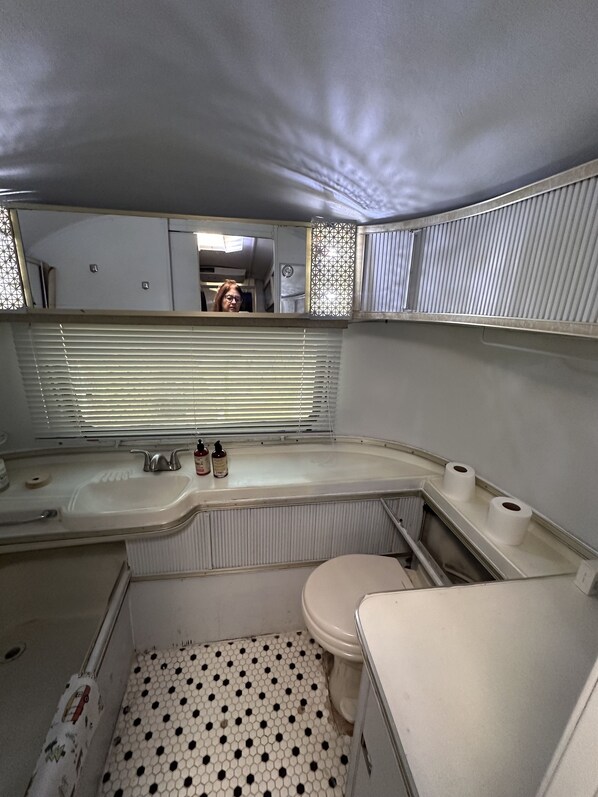 A compact bathroom with a white sink, toilet, and bathtub. There are two bottles on the sink counter, and the floor has a black and white hexagonal tile pattern.