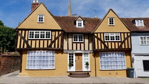 Una casa tradicional de estilo Tudor con fachada simétrica, dos chimeneas y una puerta central con un pequeño porche.