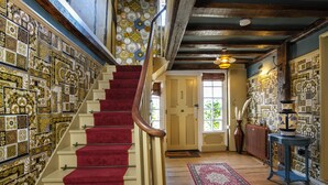 Una escalera con alfombra roja, barandilla de madera y pared con azulejos decorativos.