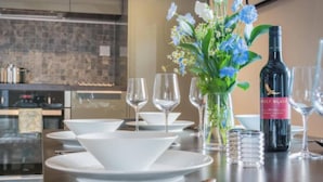 A dining table set with white plates, bowls, and wine glasses, a bottle of wine, and a vase with flowers. - Sedbergh Penthouse - KingBed - Tv - Wifi (Sedbergh)