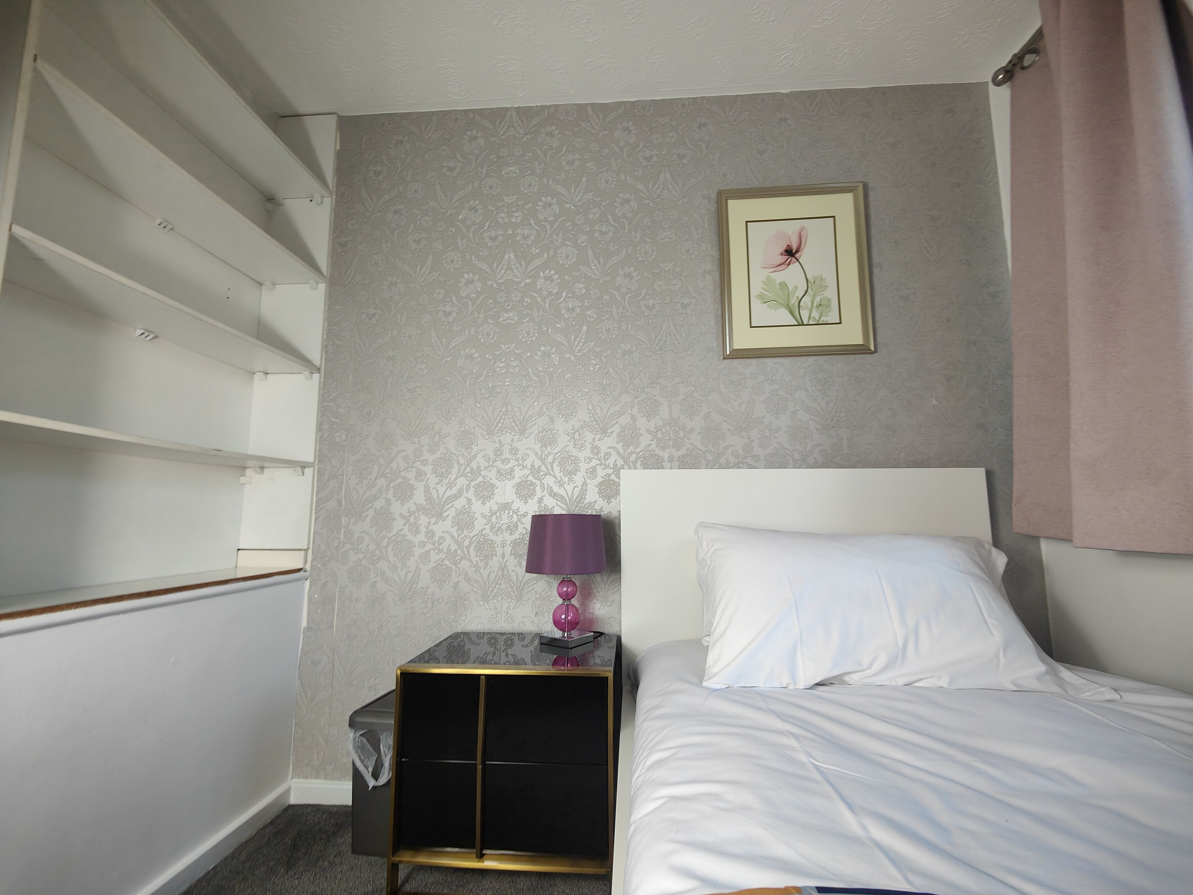 Una camera d'albergo con un letto, un comodino, una lampada e un quadro appeso al muro.