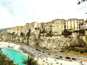 Un borgo costiero con edifici costruiti a picco sulla scogliera, una spiaggia e una strada con auto.