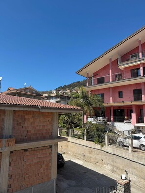 Un immeuble à plusieurs étages doté de balcons, une structure en briques au premier plan et un ciel bleu dégagé.