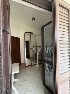 A room with a sliding glass door, a white chair, a bed, a fan, and a wardrobe.