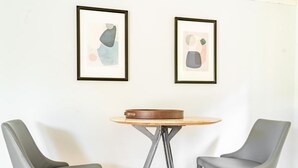 A room with two grey chairs, a round wooden table, and two framed abstract artworks on the wall. - Delightful Urban Retreat (Seattle)