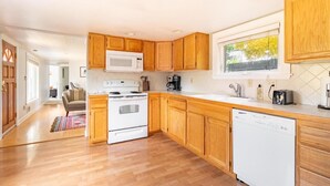 A modern kitchen with wooden cabinets, a white stove, a microwave, and a dishwasher. - Delightful Urban Retreat (Seattle)